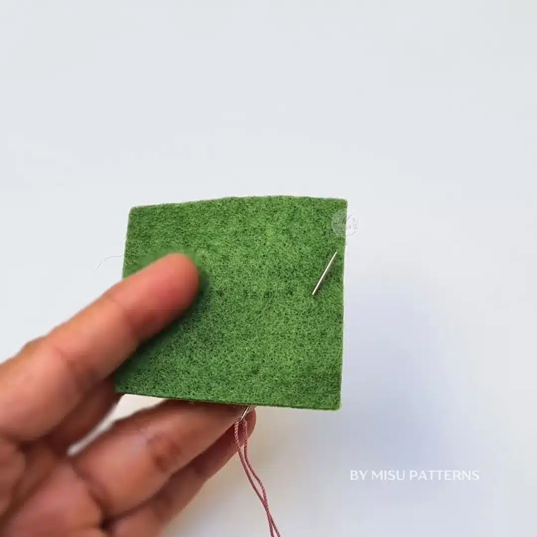 Close-up of an embroidery needle coming up through felt from the back to the front at the start of a line.